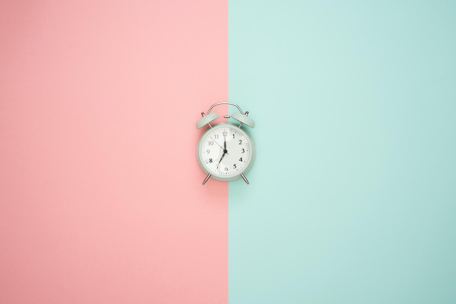 Clock lying on pink and blue pastel background