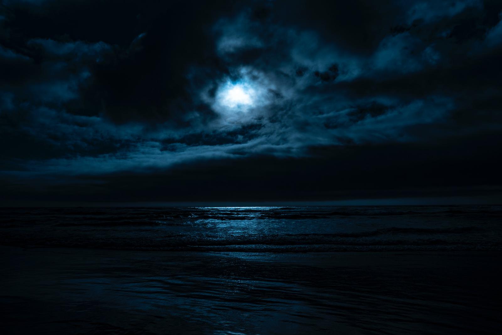 A view of the expansive sea on a cloudy night with a bright moon